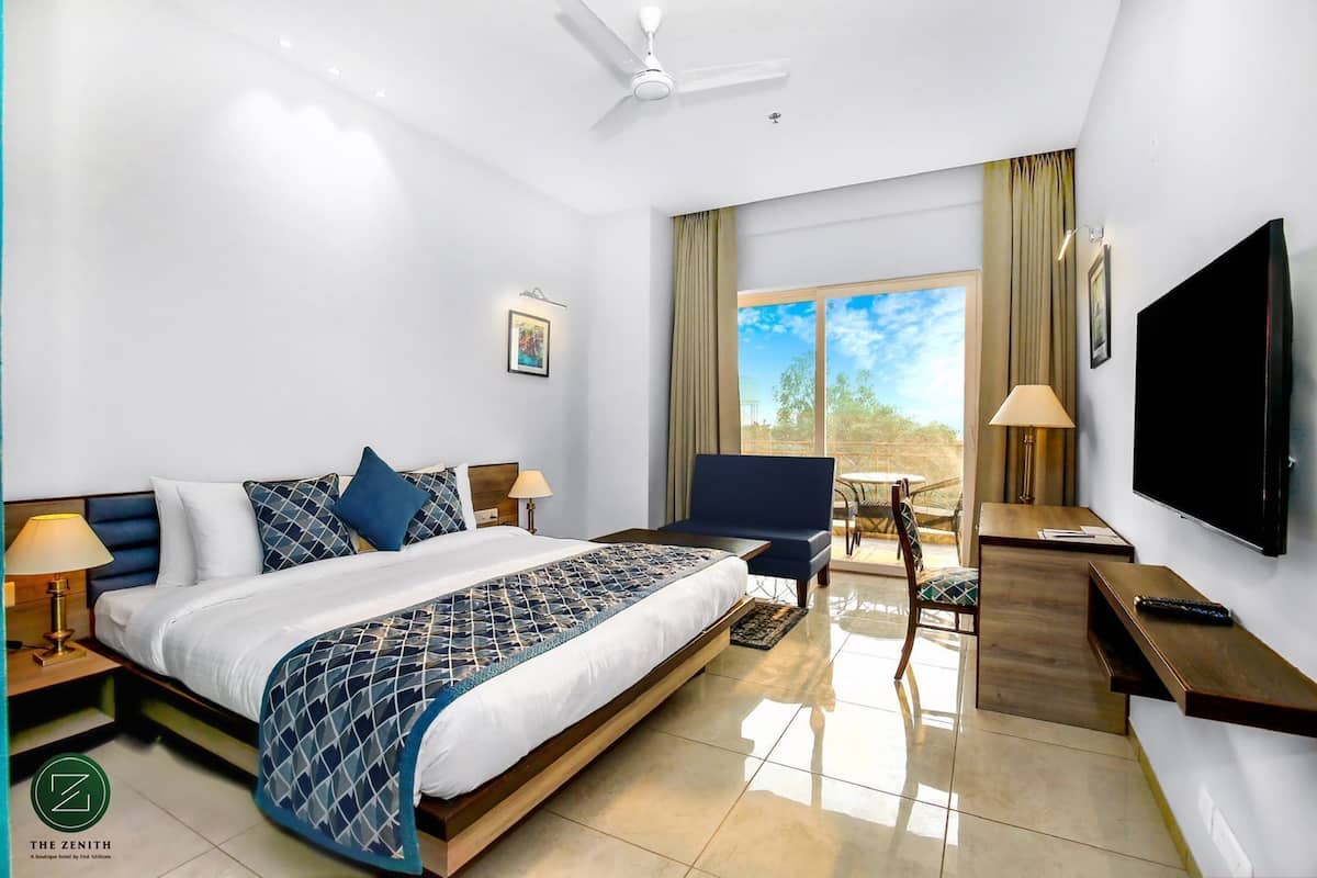 Une chambre d’hôtel comprenant un lit, un bureau, une chaise, une télévision et un balcon avec une table et des chaises.