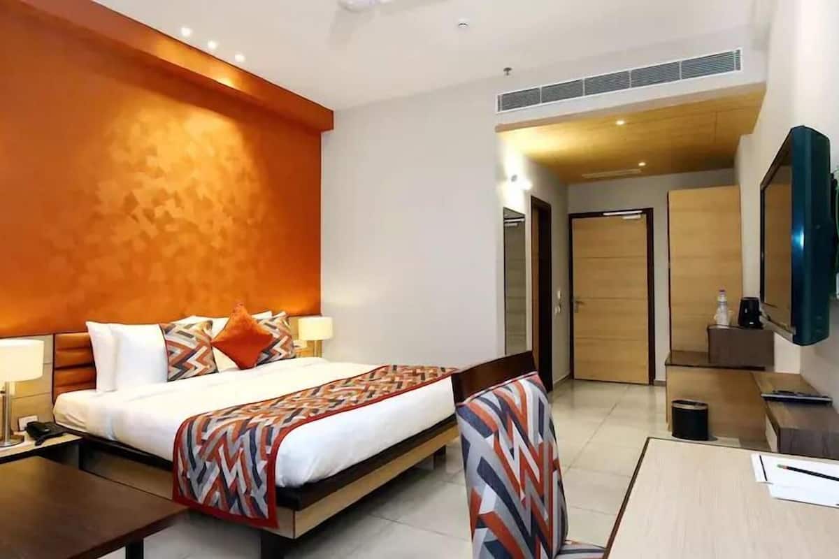 Une chambre d’hôtel comprenant un lit, des tables de chevet, un bureau, une chaise, une télévision et une porte donnant sur une autre pièce.