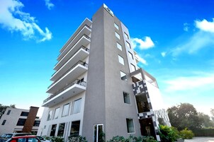 Un hotel de varios pisos con diseño moderno, que cuenta con balcones en cada planta y una entrada destacada con fachada de vidrio.