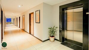 Un pasillo de hotel con un ascensor moderno, obras de arte enmarcadas en las paredes y una planta en maceta.