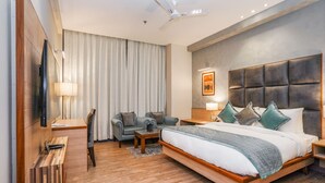 Una habitación de hotel moderna con una cama grande, una zona de estar con dos sillones, un escritorio y un televisor de pantalla plana.