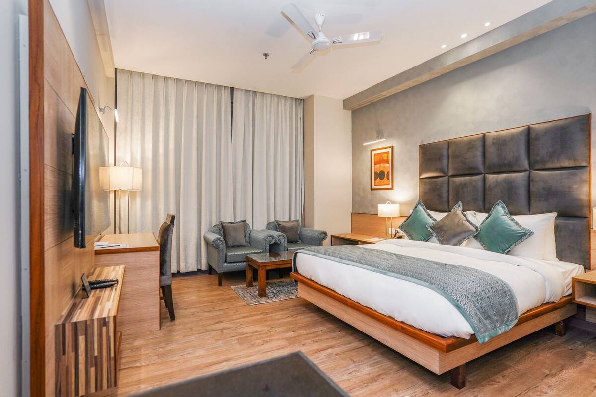 Une chambre d’hôtel moderne dotée d’un grand lit, d’un coin salon avec deux fauteuils, d’un bureau et d’une télévision à écran plat.