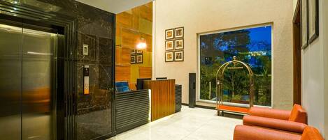 A hotel lobby with a reception desk, a reception area, a seating area, and a large window with a view of trees.