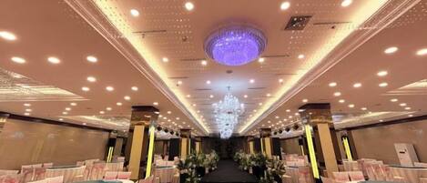 A banquet hall with round tables, a central stage, and a chandelier.