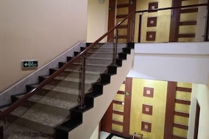 Un interior de varios niveles con una escalera, un detector de incendios y una pared con un diseño geométrico.