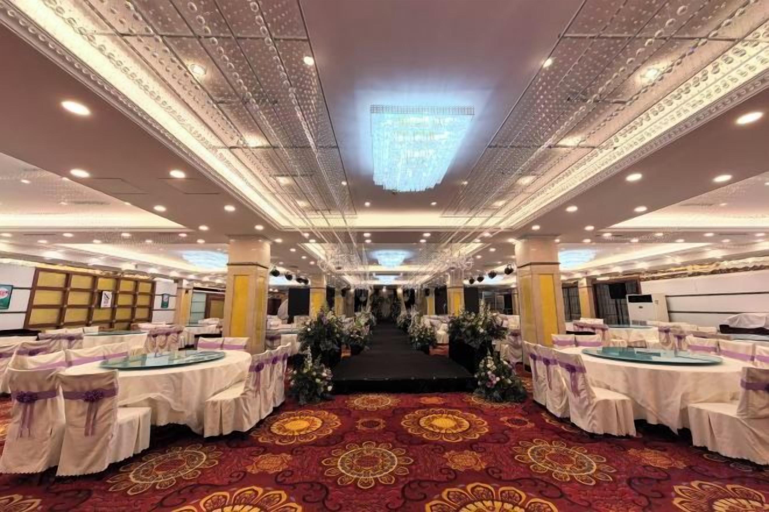 A banquet hall with round tables, a red carpet, and a chandelier.
