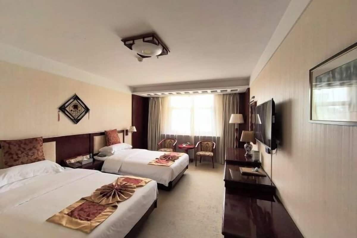 A hotel room with two beds, a TV, a desk, and a window with curtains.