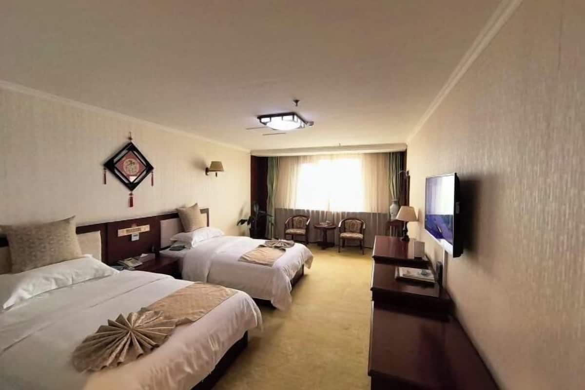 A hotel room with two beds, a television, a desk, a chair, a lamp, and a window with curtains.