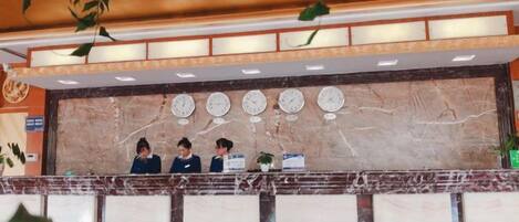Una recepción de hotel con mostrador de mármol, tres empleados y un reloj de pared.