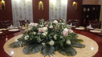 A round table with a floral centerpiece surrounded by chairs, set in a room with patterned wallpaper and wall sconces.