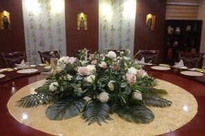 A round table with a floral centerpiece surrounded by chairs, set in a room with patterned wallpaper and wall sconces. - Cuilinyuan Hotel (Zibo)