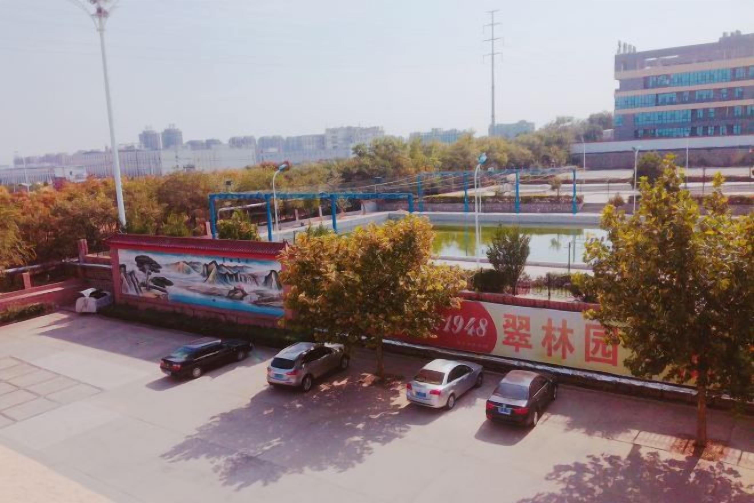 A parking area with cars, a mural, and a building in the background.
