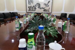 A conference room with a long table, chairs, water bottles, a potted plant, and a painting on the wall. - Cuilinyuan Hotel (Zibo)