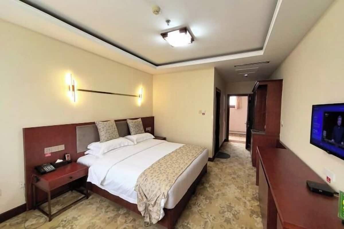 A hotel room with a large bed, bedside table, lamp, and a television on a stand.