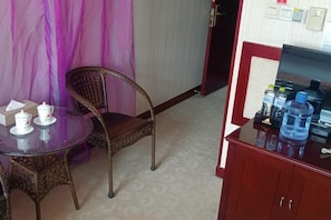 A small room with a round glass table, wicker chairs, a red cabinet with water bottles, and a purple curtain.