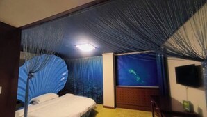 A room with a bed, a television, and a wall-mounted screen displaying an underwater scene. - Cuilinyuan Hotel (Zibo)