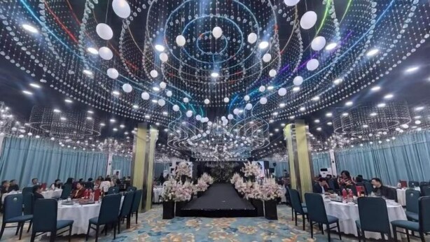 A banquet hall with round tables, a stage, and a ceiling adorned with hanging lights. - Cuilinyuan Hotel (Zibo)