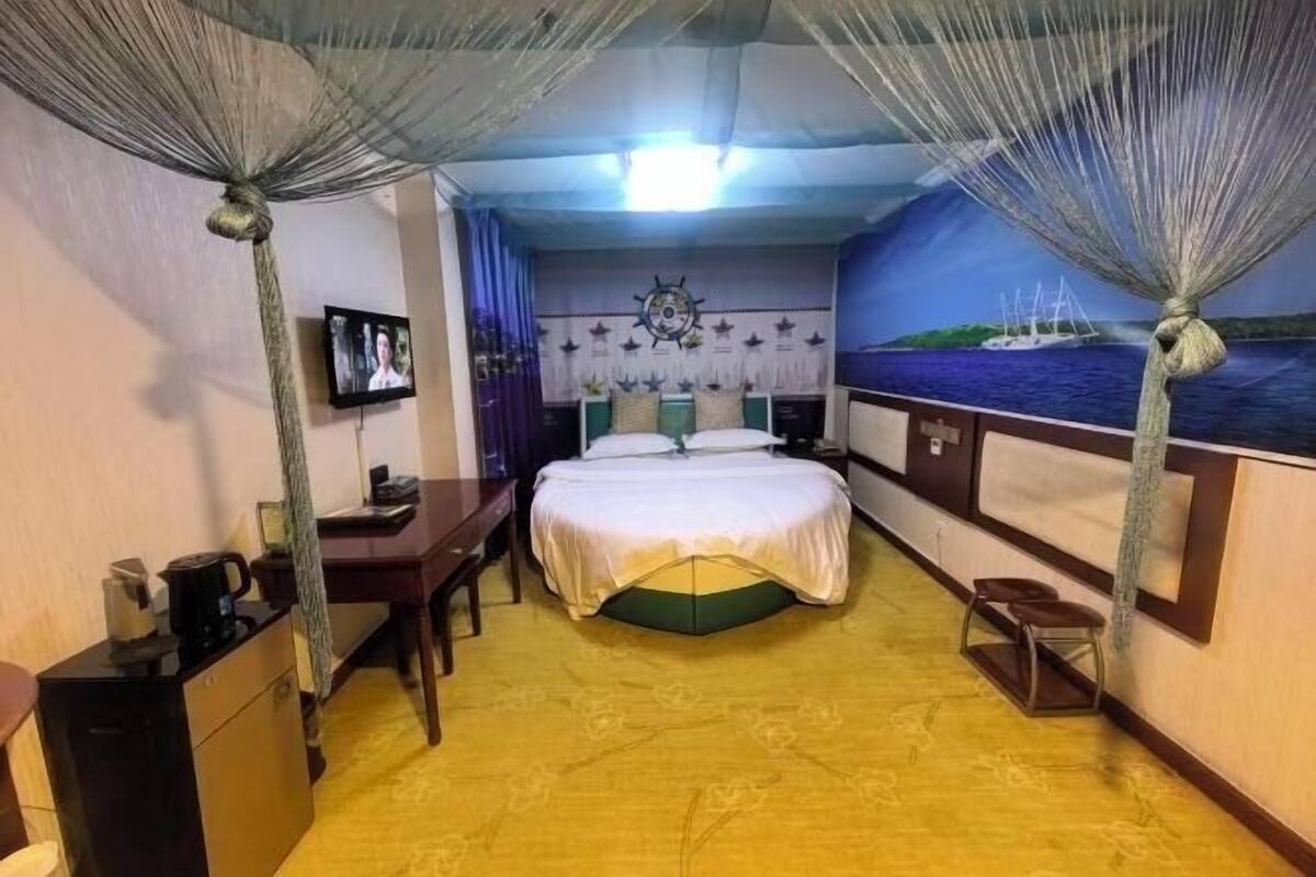 A bedroom with a bed, desk, chair, and a TV.