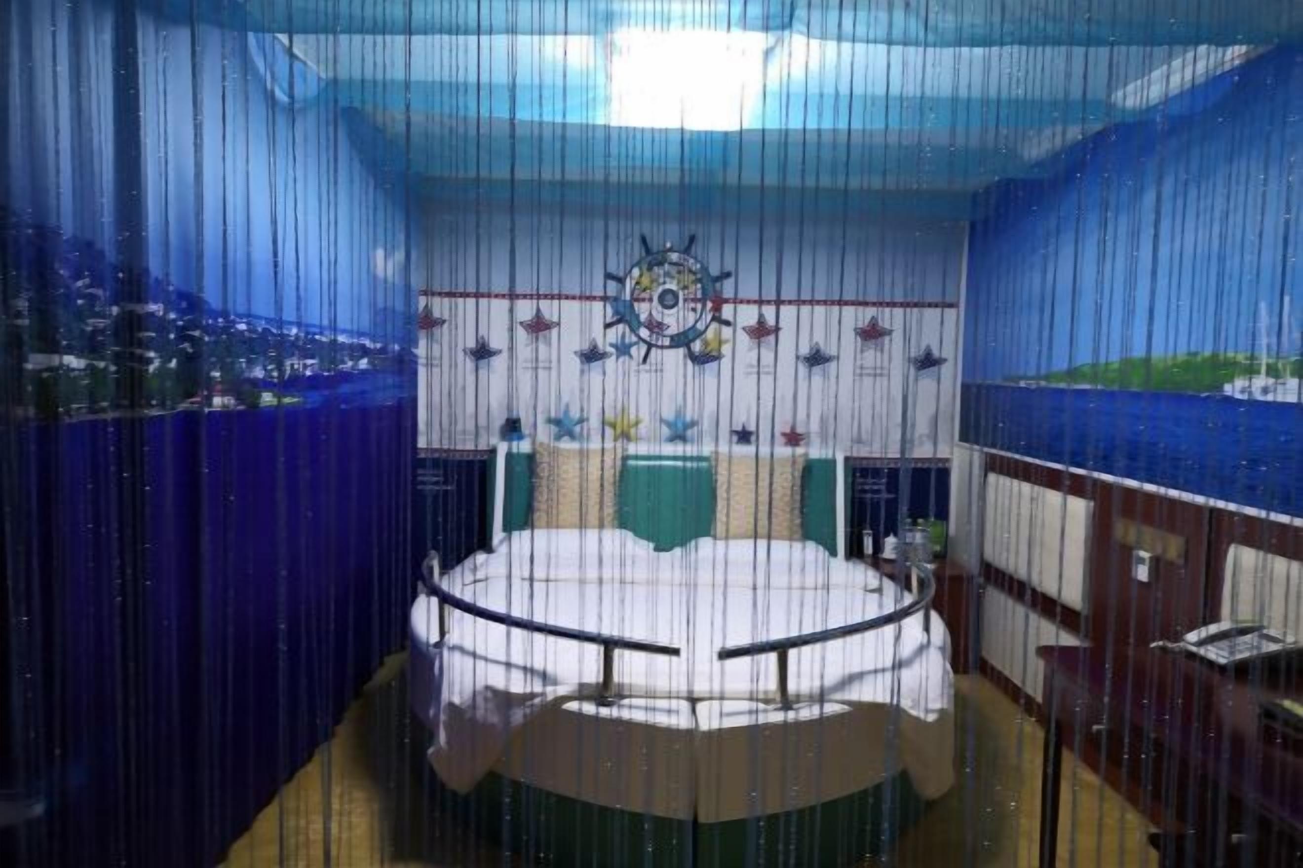A circular room with a central table, a ship's wheel decoration, and a view of a coastal landscape through the windows.