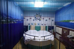Una habitación circular con una mesa en el centro, un adorno con timón de barco y vistas a un paisaje costero a través de las ventanas.