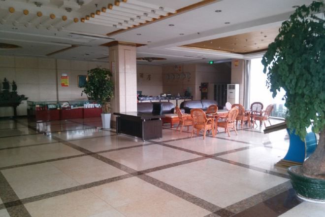A spacious lobby with a check-in counter, seating area, and large potted plants.