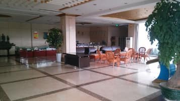 A spacious lobby with a check-in counter, seating area, and large potted plants.
