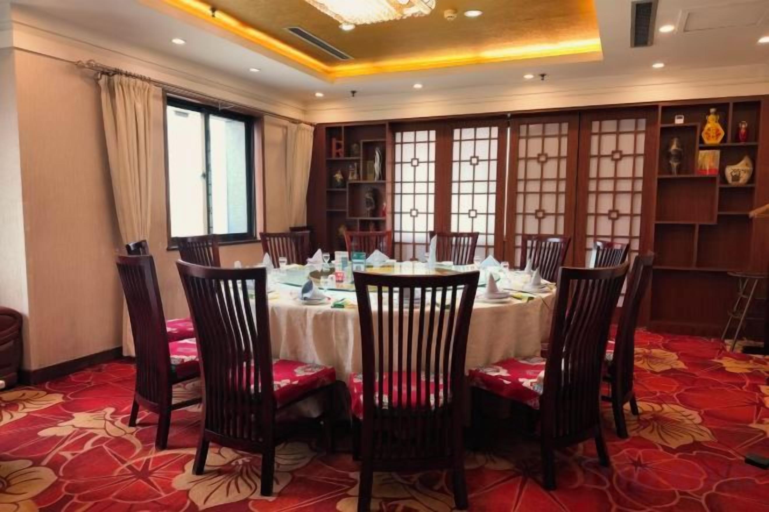 A dining area with a round table set for six, surrounded by chairs, with a patterned carpet and traditional decor.