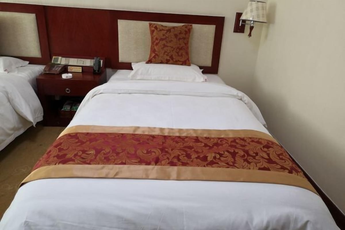 A hotel room with a large bed, a bedside table with a phone and a lamp, and a headboard with a decorative panel.