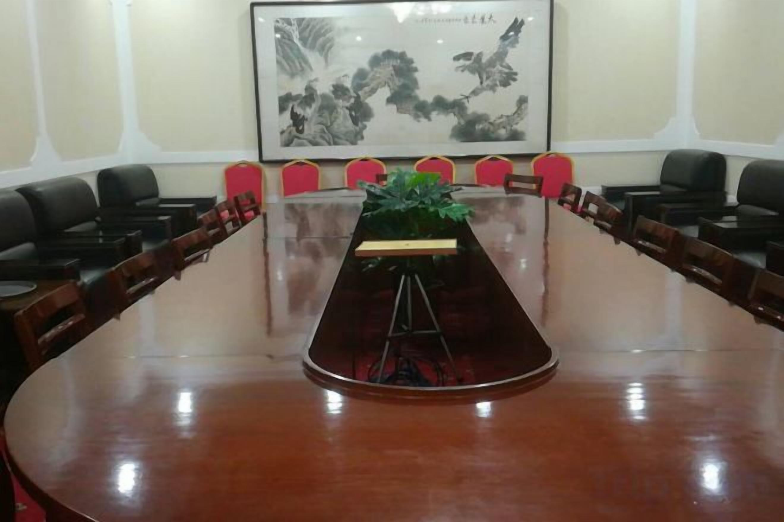 Un salón de conferencias con una larga mesa, sillas y una planta.