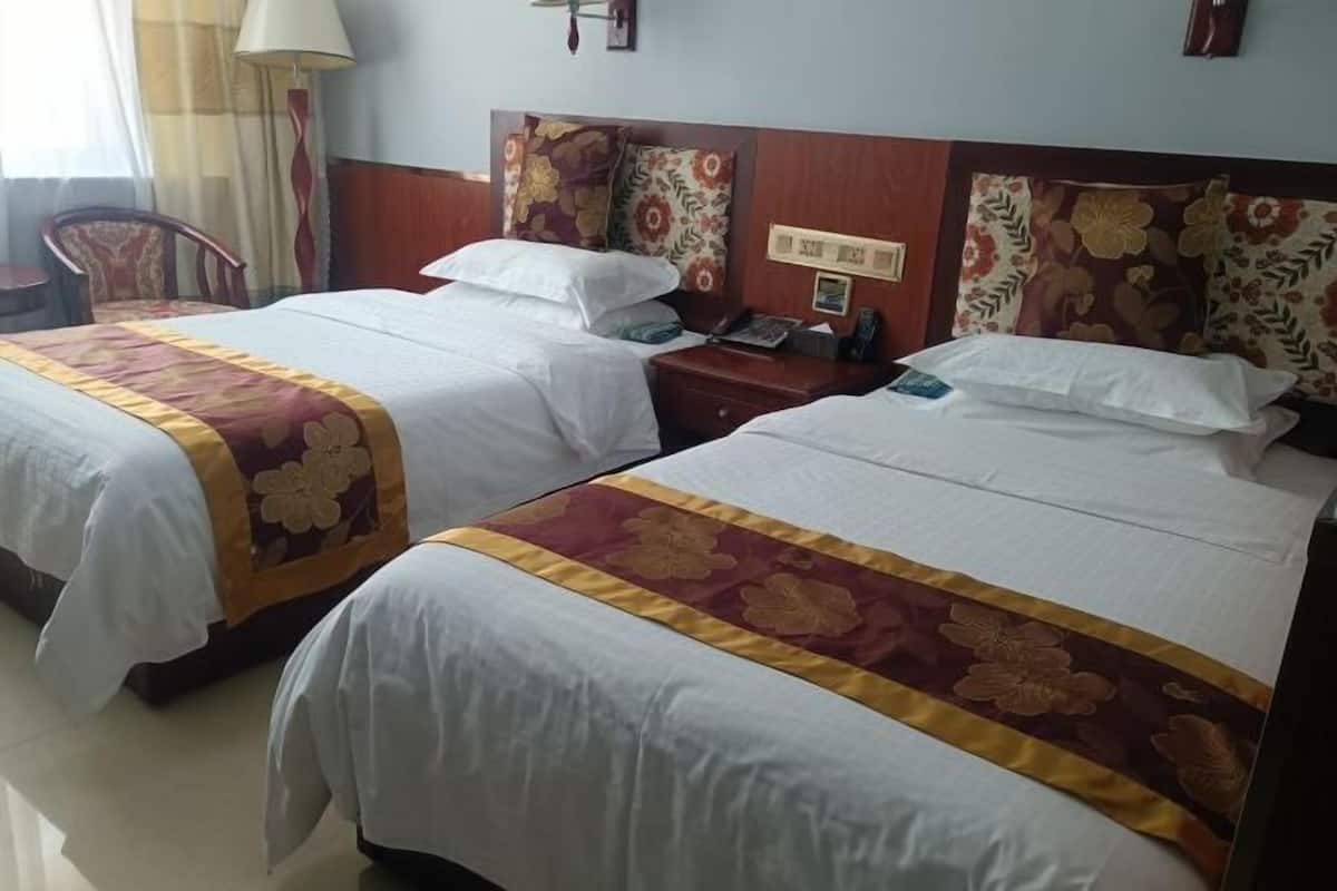 Two single beds with floral bedspreads, a wooden headboard, a nightstand with a lamp, and a chair.