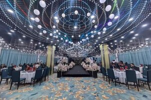 Un salón de banquetes con mesas dispuestas para cenar, un escenario al frente y un techo decorado con luces colgantes.