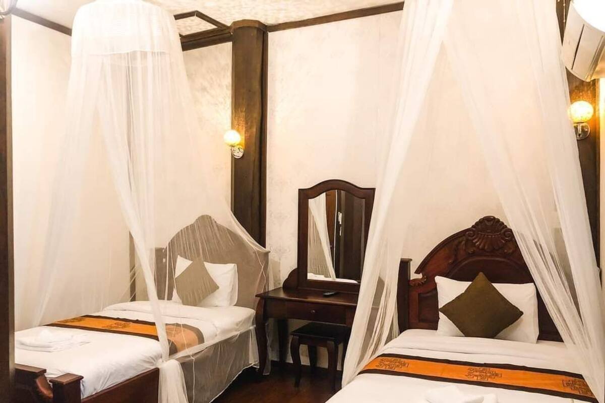 Dos camas individuales con dosel, una mesita de noche de madera, una silla y un espejo colgado en la pared.