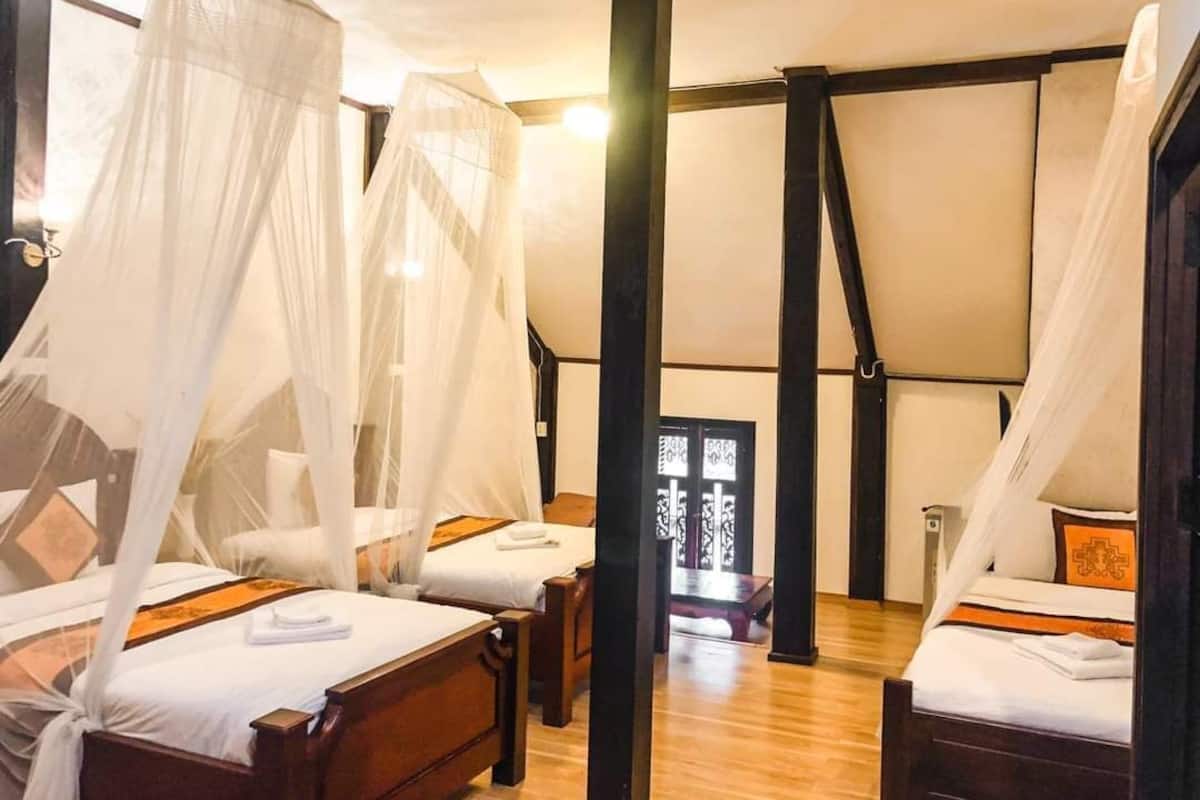 Una habitación con cuatro camas, cada una con dosel. El suelo es de madera y el techo es inclinado.