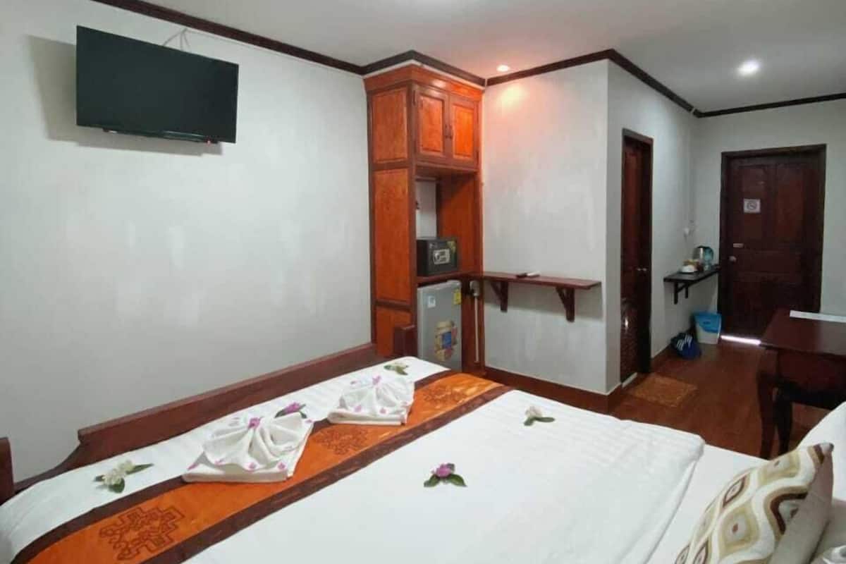 Una habitación de hotel con una cama, un televisor montado en la pared, un armario de madera y un escritorio.