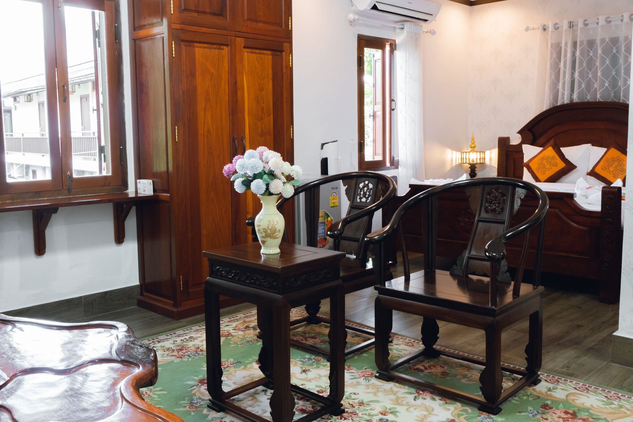 A traditional room with wooden furniture, a floral-patterned rug, and a bed with a headboard.