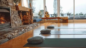 A cozy living room with a stone fireplace, yoga mats, and a guitar. - Ora Retreat (Queenstown)