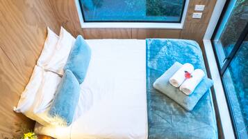 Un dormitorio pequeño con cama, almohadas, una mesita de noche con lámpara y ventana con vistas a zonas verdes.