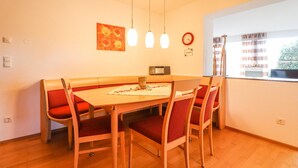 A dining area with a wooden table and red cushioned chairs, a clock, and pendant lights.
