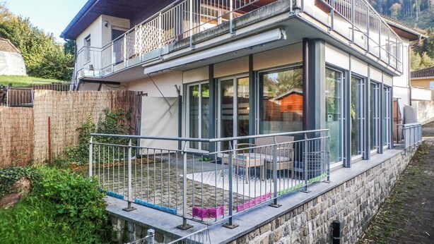 A modern house with a glass balcony, a stone foundation, and a view of the surrounding landscape.