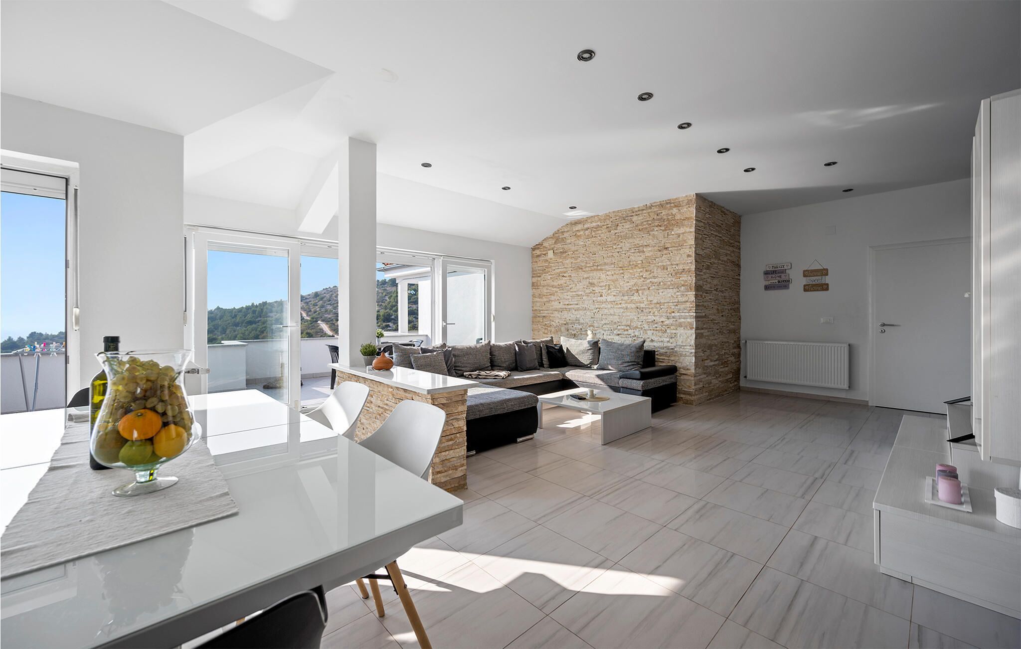 A modern living room with a stone accent wall, a dining area with a glass table, and a view of the outdoors.