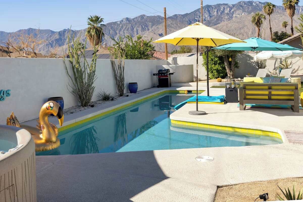 Sunny backyard with lap pool, yellow-tile edge, patio seating, gas grill, and mountain views — pool floats included, relaxation mandatory