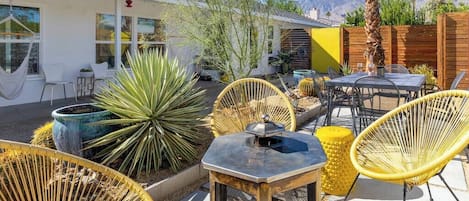 An outdoor patio with wicker chairs, a table, and a potted plant.