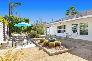 A patio with outdoor furniture, a cactus garden, and a white building with large windows.