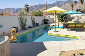 A swimming pool with a mountain backdrop, a hot tub, and outdoor seating with umbrellas.