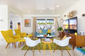 Un salon moderne avec un canapé, des fauteuils jaunes, une table basse et un téléviseur.