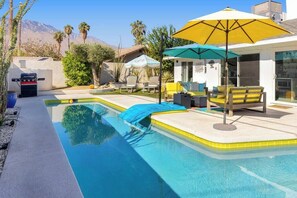 Un área de piscina con una parrilla, mobiliario exterior y sombrillas.
