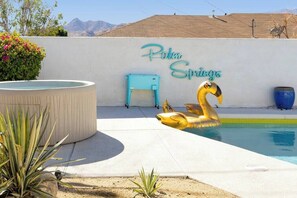 A swimming pool with a swan float, a hot tub, and a wall with the text "Palm Springs".