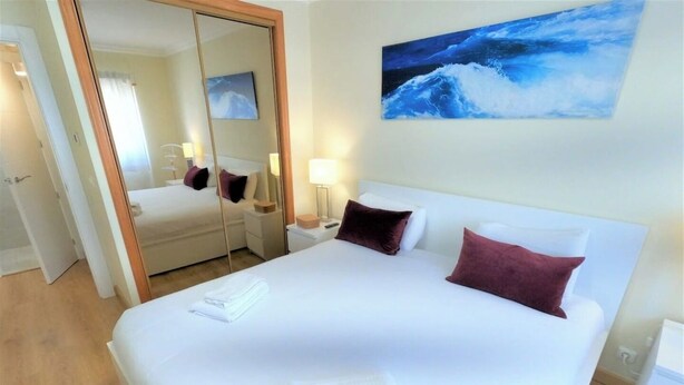 A hotel room with a large bed, a mirror, a painting of waves, and a wooden floor. - Carnaxide, modern T1 apartment w/ balcony, Lisbon (Carnaxide)