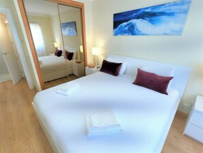 A hotel room with a large bed, a mirror, a painting of waves, and a wooden floor.