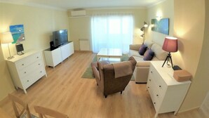 A living room with a TV, sofa, chairs, a coffee table, and a lamp. - Carnaxide, modern T1 apartment w/ balcony, Lisbon (Carnaxide)